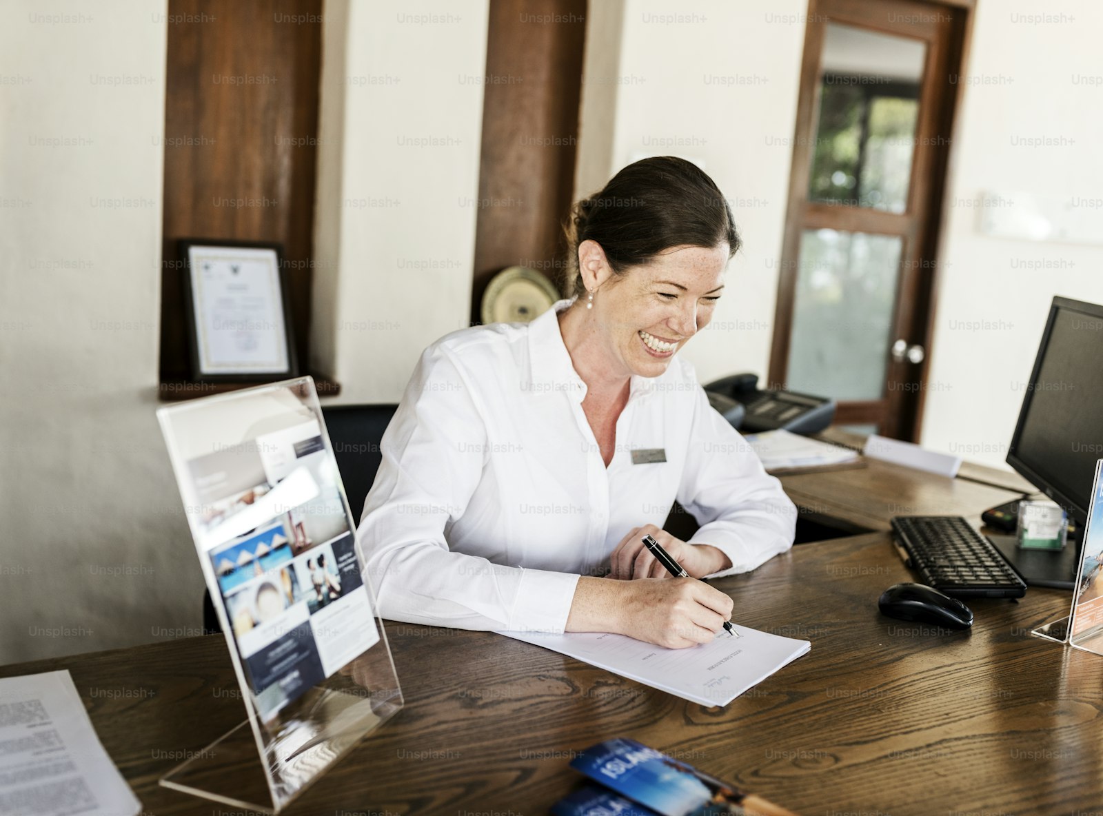 Person writing at a front desk beside a computer and telephone